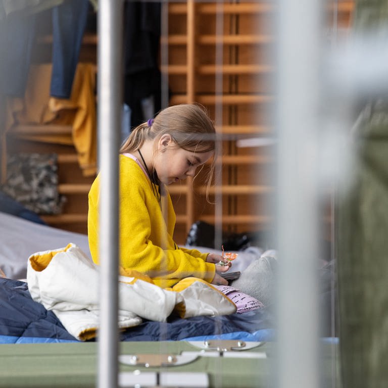 Ein neunjähriges Mädchen aus der Ukraine sitzt in der Notunterkunft in Bad Kreuznach auf ihrem Feldbett. (Foto: dpa Bildfunk, Picture Alliance)