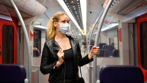 Frau steht in einem Zug und hat eine medizinische Maske an.  (Foto: picture-alliance / Reportdienste, picture alliance / imageBROKER | Michael Weber)