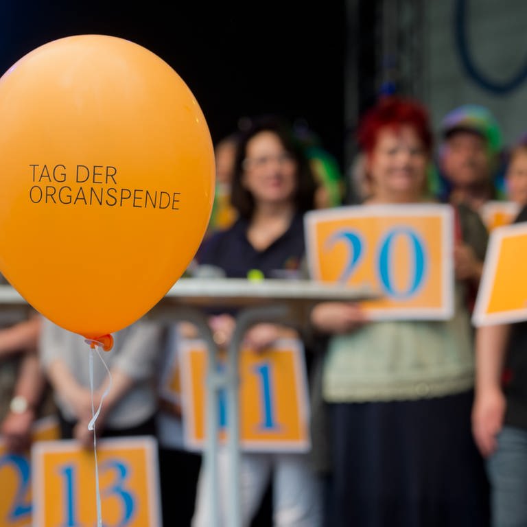 Ein Luftballon auf dem "Tag der Organspende" steht, dahinter Menschen die Schilder in die Höhe halten (Foto: dpa Bildfunk, picture alliance / dpa | Julian Stratenschulte)