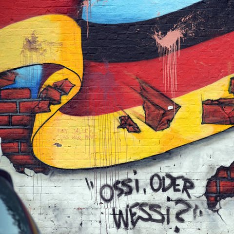 Passanten gehen an einem Graffiti mit der deutschen Nationalflagge und dem Schriftzug "Ossi oder Wessi? vorbei. (Foto: dpa Bildfunk, Picture Alliance)