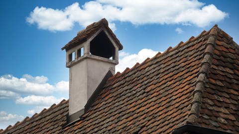 Schornstein mit Regenschutz auf einem terracottafarbenen Dach. (Foto: IMAGO, IMAGO / Shotshop)