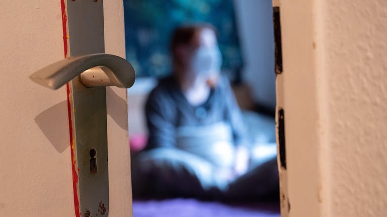 Eine Frau sitzt während der Isolation nach einem positiven Corona-PCR-Test auf ihrem Bett. (Foto: dpa Bildfunk, Picture Alliance)