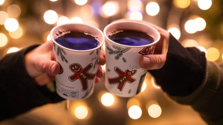 Zwei Personen stoßen mit Glühwein gefüllten Bechern auf dem Weihnachtsmarkt an. (Foto: dpa Bildfunk, Picture Alliance)