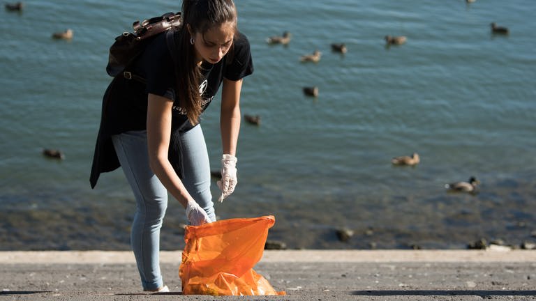 Eine Ehrenamtliche sammelt am Rheinufer Müll zusammen. (Foto: picture-alliance / Reportdienste, dpa | Silas Stein)