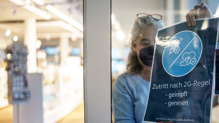 Frau holt 2G-Schild aus Schaufenster. Rheinland-Pfalz will 2G im Einzelhandel kippen (Foto: dpa Bildfunk, picture alliance/dpa | Axel Heimken)