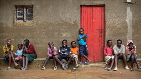 Ruandische Kinder sitzen vor einem Lehmhaus mit einer roten Tür (Foto: picture-alliance / Reportdienste, picture alliance/dpa | Ben Curtis)