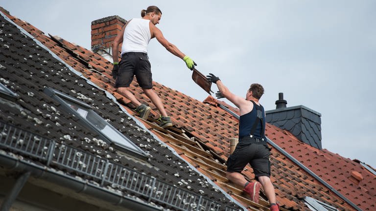 Zwei Dachdecker reichen sich auf einem Dach Ziegel an.  (Foto: dpa Bildfunk, picture alliance/dpa | Silas Stein)