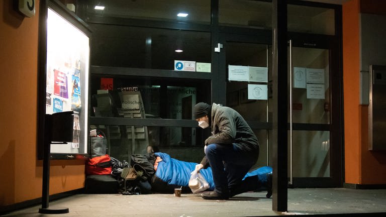Mann bringt ein Lunchpaket und heißen Tee zu einem Obdachlosen in seinem Schlafsack (Foto: picture-alliance / Reportdienste, Picture Alliance)