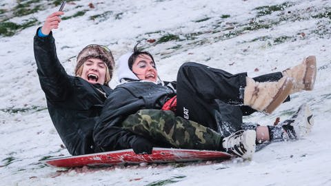 Spaß im Schnee: Ein jungen Paar rutscht einen Hügel hinunter  (Foto: picture-alliance / Reportdienste, Picture Alliance)