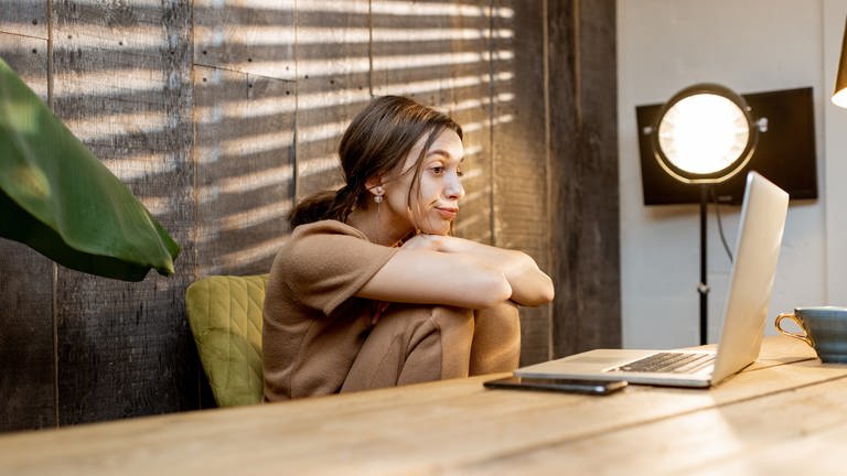 Eine Frau sitzt im Homeoffice und schaut gelangweilt auf ihren Laptop. (Foto: Adobe Stock)