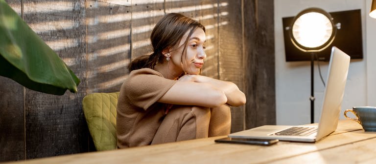 Eine Frau sitzt im Homeoffice und schaut gelangweilt auf ihren Laptop. (Foto: Adobe Stock)