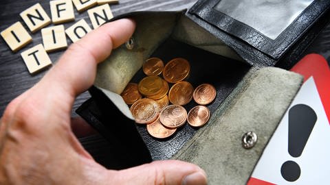 Hand öffnet Portemonnaie mit Kleingeld, Schriftzug Inflation und Gefahrenschild (Foto: IMAGO, IMAGO / Christian Ohde)