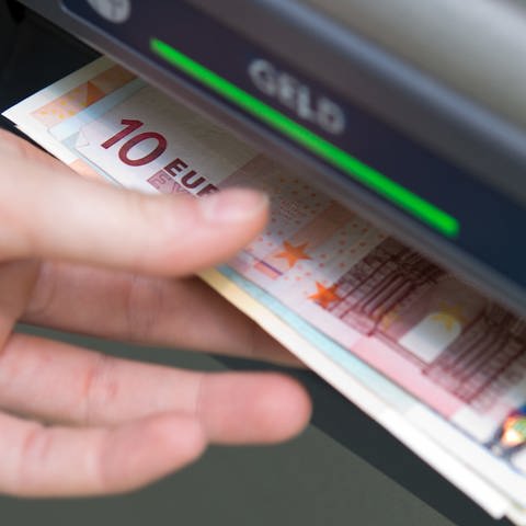 Eine Hand greift nach Geldscheinen, die aus einem Geldautomaten ausgeworfen wurden.  (Foto: dpa Bildfunk, picture alliance/dpa | Andrea Warnecke)