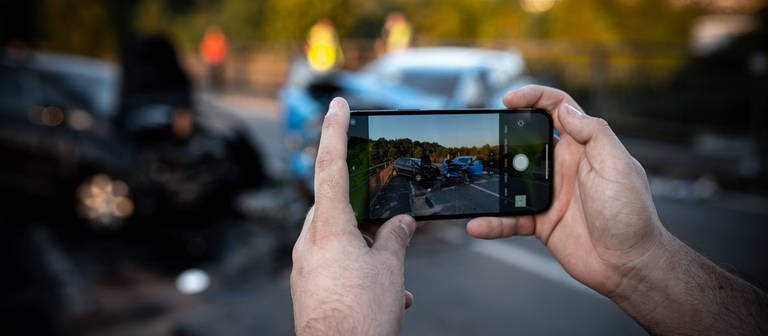 Ein Gaffer macht mit seinem Smartphone Bilder von einer Unfallstelle. (Foto: IMAGO, IMAGO / vmd-images)