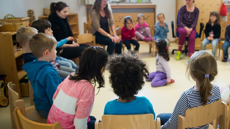 Kinder und Erzieherinnen sitzen in einer Kita im Kreis.  (Foto: dpa Bildfunk, Monika Skolimowska)