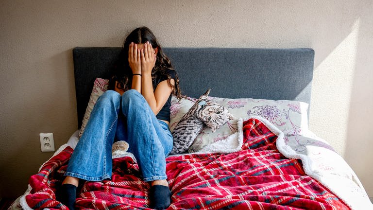 Jugendliches Mädchen mit Depression sitzt auf ihrem Bett und hält sich die Hände vors Gesicht (Foto: dpa Bildfunk, picture alliance / ROBIN UTRECHT | Robin Utrecht)