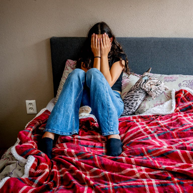 Jugendliches Mädchen mit Depression sitzt auf ihrem Bett und hält sich die Hände vors Gesicht (Foto: dpa Bildfunk, picture alliance / ROBIN UTRECHT | Robin Utrecht)