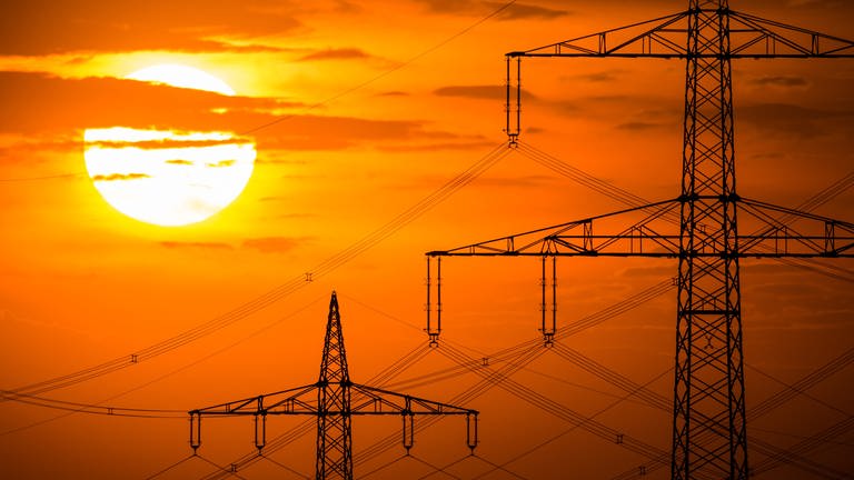 Die Sonne geht hinter Strommasten unter: Die Energiepreise in Europa steigen derweil. (Foto: dpa Bildfunk, picture alliance/dpa | Arne Immanuel Bänsch)