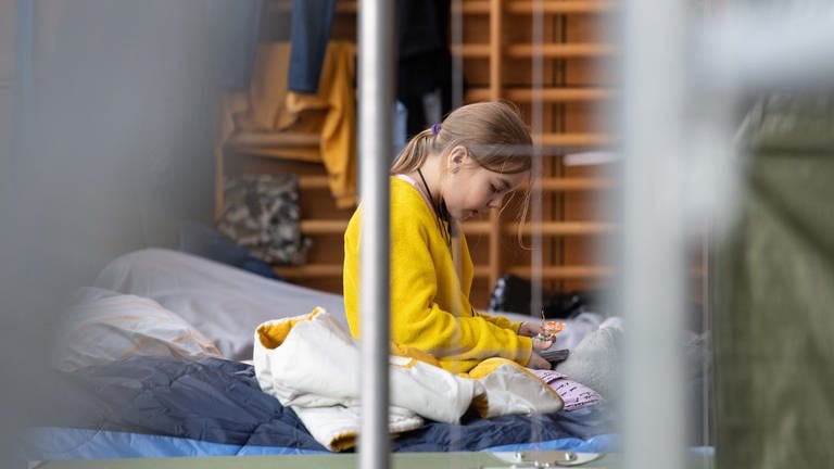 Ein neunjähriges Mädchen aus der Ukraine sitzt in der Notunterkunft in Bad Kreuznach auf ihrem Feldbett. (Foto: dpa Bildfunk, Picture Alliance)