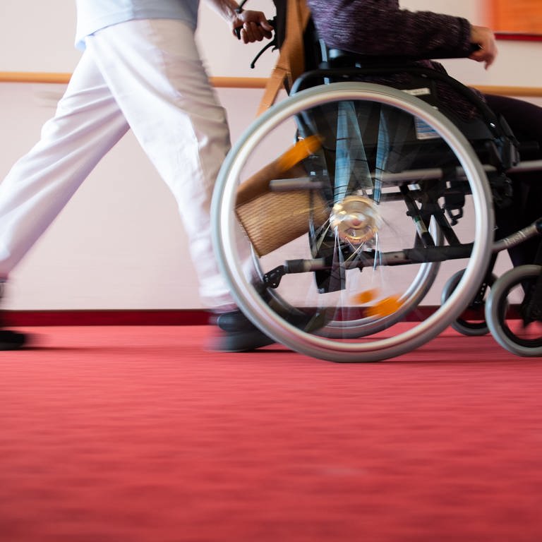 Ein Pfleger eines Pflegeheims schiebt eine Bewohnerin mit einem Rollstuhl.  (Foto: dpa Bildfunk, picture alliance/Tom Weller/dpa)