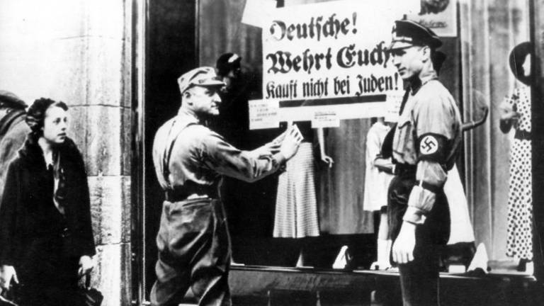 SA-Männer kleben während des Dritten Reiches ein volksverhetzendes Plakat mit der Aufschrift "Deutsche! Wehrt Euch! Kauft nicht bei Juden" an der Schaufensterscheibe eines Geschäfts (undatiertes Archivfoto). (Foto: picture-alliance / dpa)