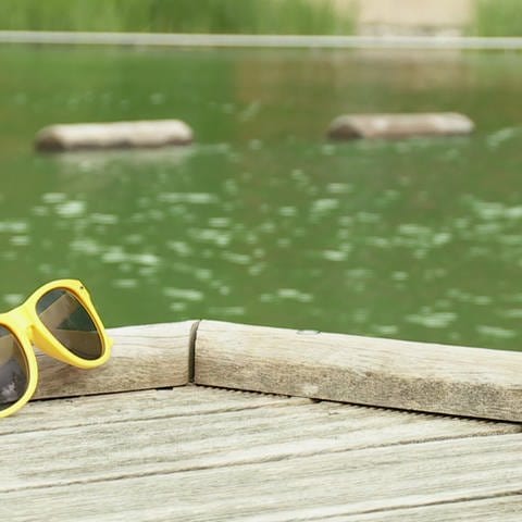 Gelbe Sonnenbrille liegt an einem Schwimmbad