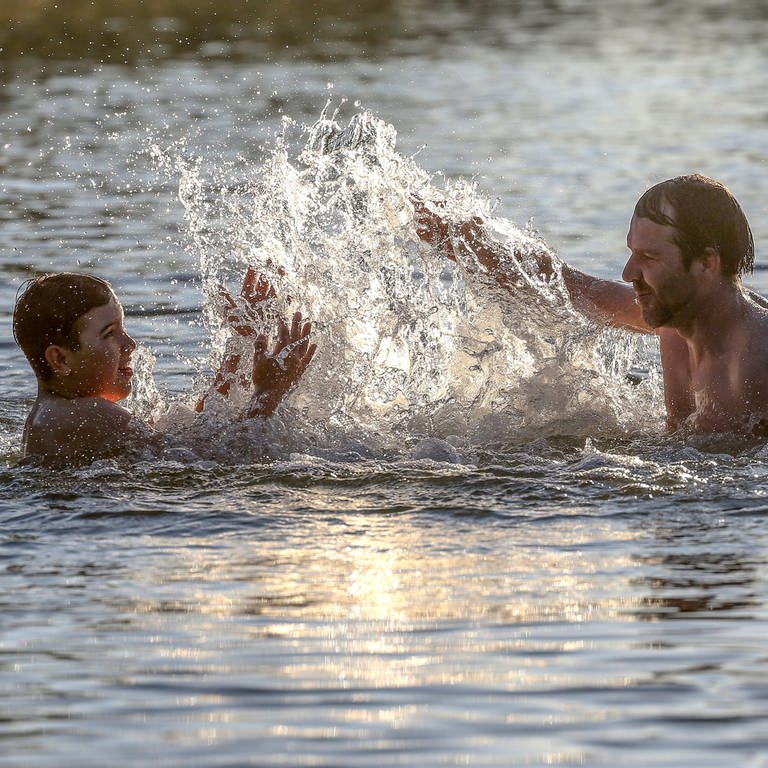 Ein Vater und sein Sohn spritzen sich in einem Badesee mit Wasser an. (Foto: dpa Bildfunk, picture alliance/dpa | Thomas Warnack)