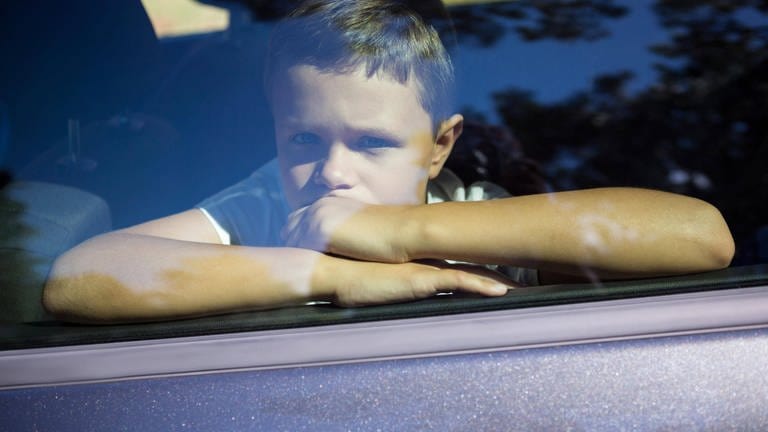 Ein kleiner Junge sitzt im Auto hinter einer geschlossenen Scheibe.