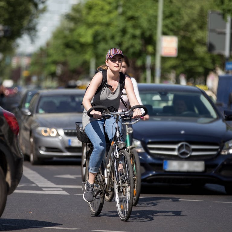Zwei Fahrradfahrerinnen bahnen sich ihren Weg zwischen den Autos.