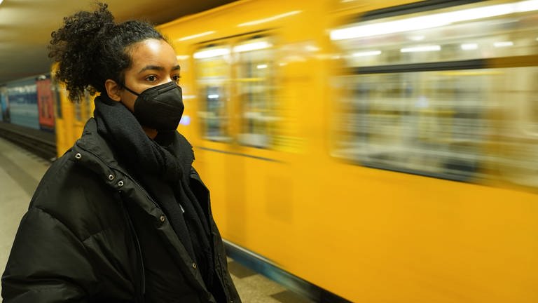 Frau mit FFP2-Maske steht vor Bahn (Foto: picture-alliance / Reportdienste, picture alliance/dpa | Jörg Carstensen)