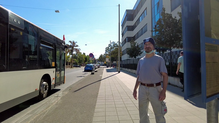 Der Bewohner des Thaddäusheims Mainz, Lorenz Franco Siegfried, steht an einer Bushaltestelle. Ein Bus hält links neben ihm. (Foto: SWR)