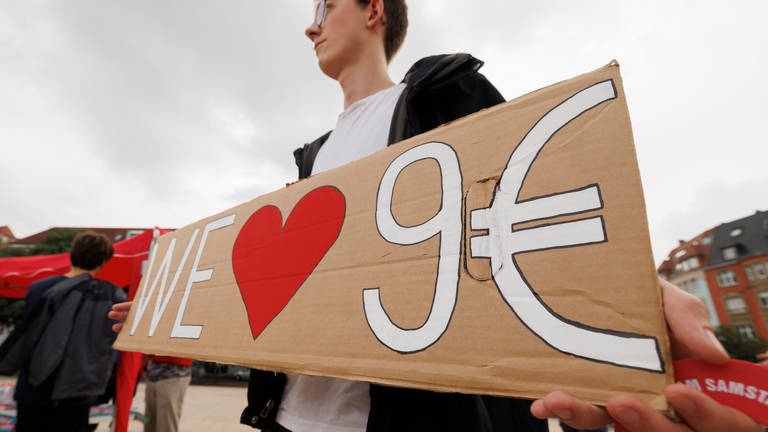 Ein junger Mann hält ein Pappschild hoch mit der Aufschrift "We Love 9 Euro" - der Landtag in RLP diskutiert über Nachfolgemodelle (Foto: dpa Bildfunk, Picture Alliance)