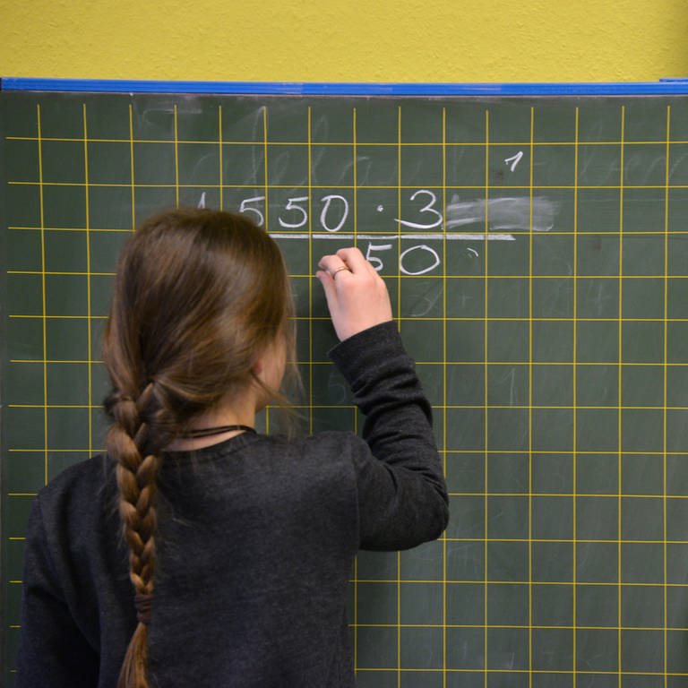 Grundschülerin rechnet an der Tafel eine Aufgabe aus.
