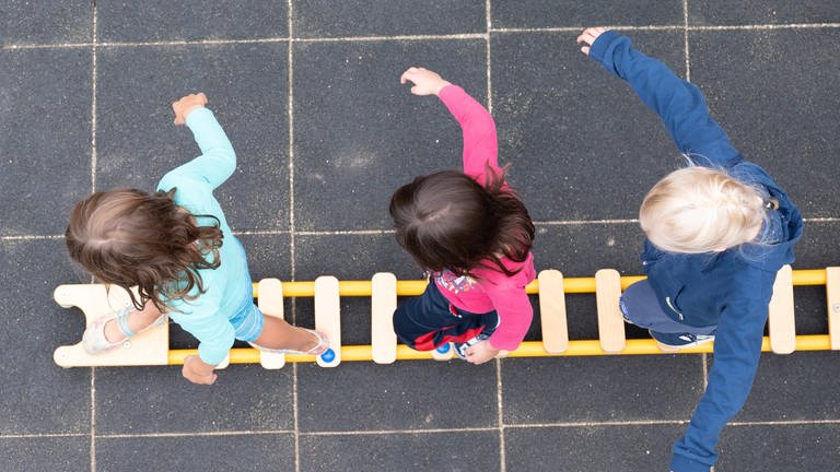 Kinder balancieren während eines Pressetermins auf dem Spielplatz einer Kindertagesstätte auf einem Brett.