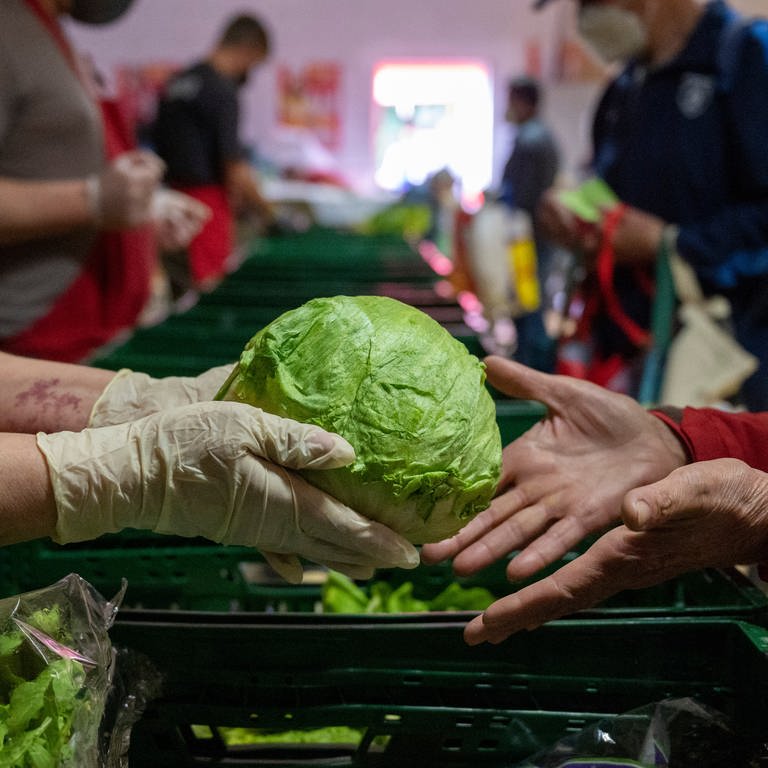 Ein Mensch überreicht einem anderen einen Salatkopf. Immer mehr Menschen in Rheinland-Pfalz sind auf Lebensmittelspenden angewiesen.