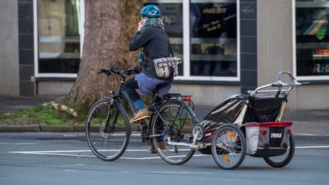 Frau fährt mit einem Fahrrad und Kinderanhänger, telefoniert während der Fahrt mit dem Handy (Foto: picture-alliance / Reportdienste, picture alliance / Jochen Tack)