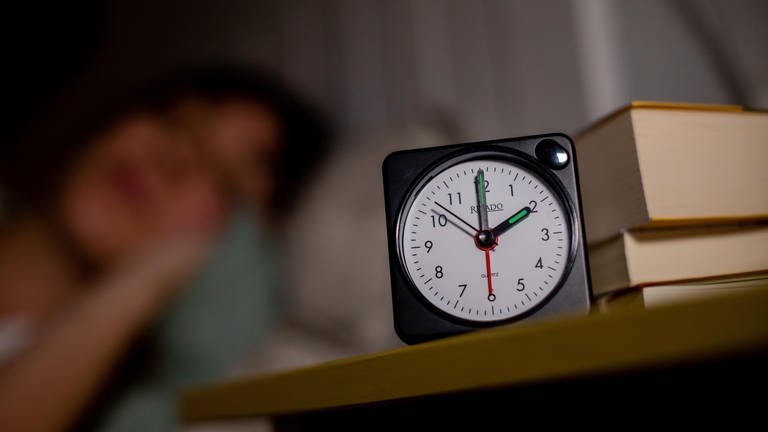 Eine Frau schläft neben einem Wecker, welcher auf 2 Uhr zeigt. Am 31.10.2021 endet die Sommerzeit (MESZ), es ist wieder mitteleuropäische Normalzeit, die umgangssprachlich auch Winterzeit genannt wird. In der Nacht zum 31. Oktober wird in Deutschland die Uhr um 3 Uhr auf 2 Uhr zurückgestellt. 
