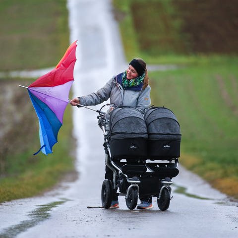 Eine Frau mit Kinderwagen versucht im stürmischen Wind ihren Regenschirm zu öffnen. (Foto: dpa Bildfunk, picture alliance/dpa | Thomas Warnack)
