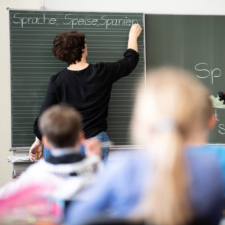 Eine Lehrerin schreibt in einer Grundschule Wörter mit "Sp" am Anfang an eine Tafel. 