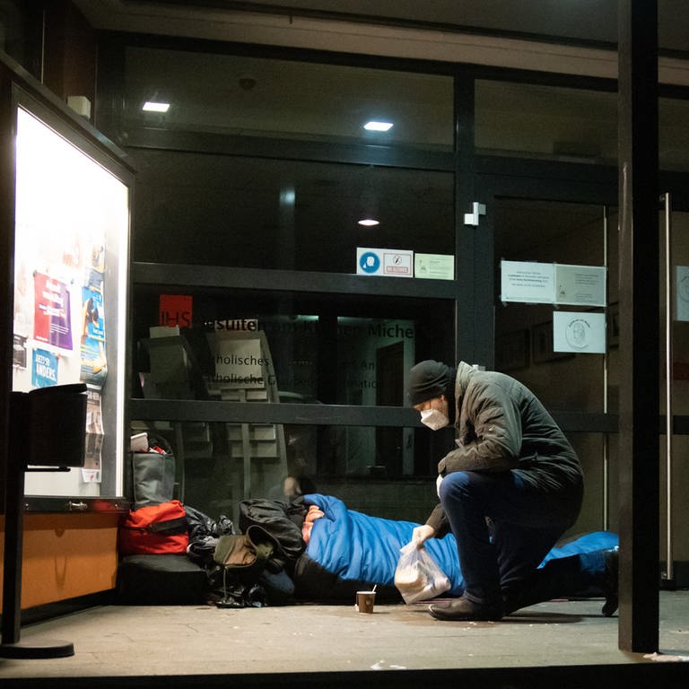Mann bringt ein Lunchpaket und heißen Tee zu einem Obdachlosen in seinem Schlafsack