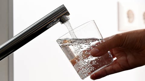 Hand mit Wasserglas unter Wasserhahn