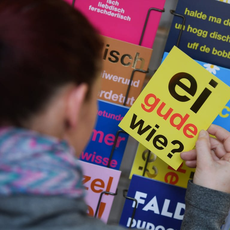 Eine Frau hält eine Postkarte mit dem klassischen hessischen Satz "Ei gude wie?" in der Hand. Jede Region hat ihre eigenen sprachlichen Einfärbungen. (Foto: dpa Bildfunk, picture alliance/dpa | Arne Dedert)