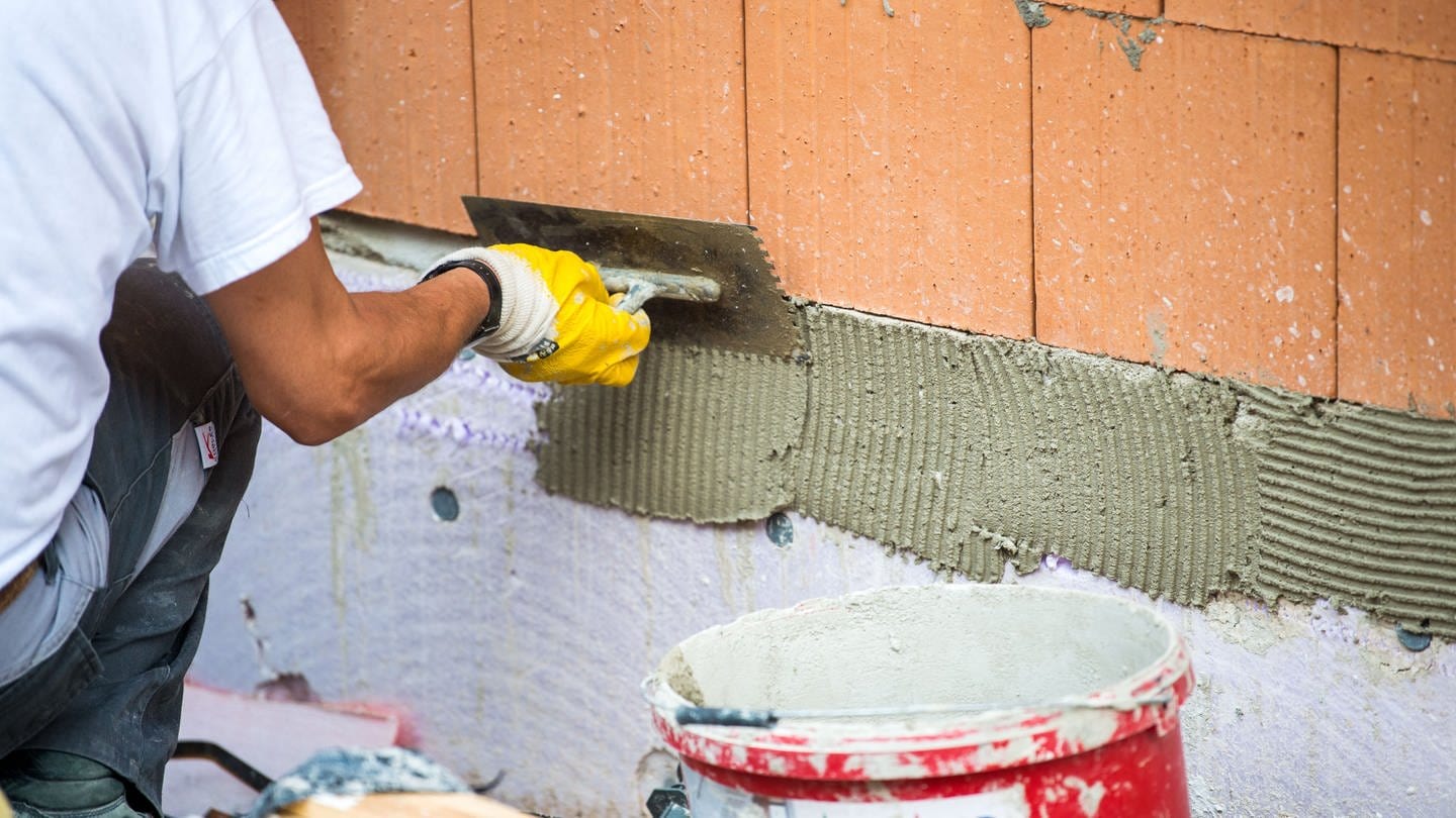 Ein Maurer trägt auf einer Baustelle Klebemörtel auf eine Wand auf. (Foto: dpa Bildfunk, Picture Alliance)