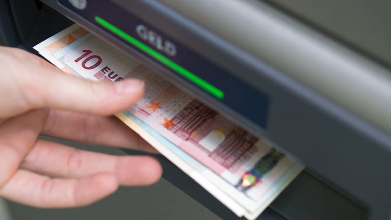 Eine Hand greift nach Geldscheinen, die aus einem Geldautomaten ausgeworfen wurden.  (Foto: dpa Bildfunk, picture alliance/dpa | Andrea Warnecke)