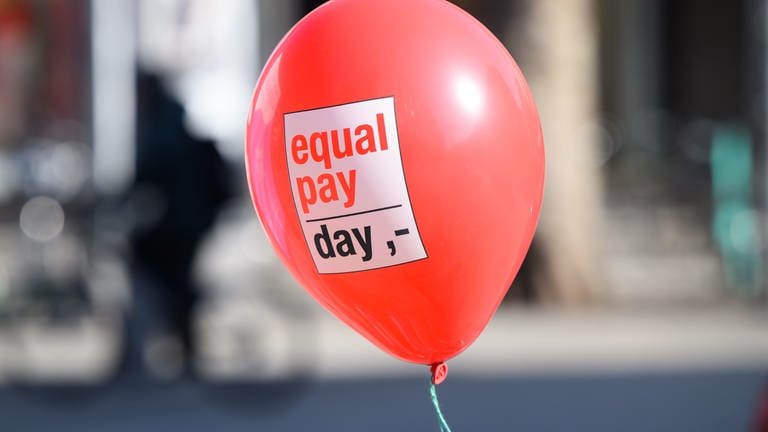 Ein Ballon mit Aufschrift „Equal Pay Day“ schwebt in der Luft.