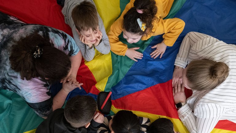 Kindergartengruppe und Erzieherinnen liegen zusammen auf einem großen Tuch  (Foto: dpa Bildfunk, picture alliance/dpa | Marijan Murat)