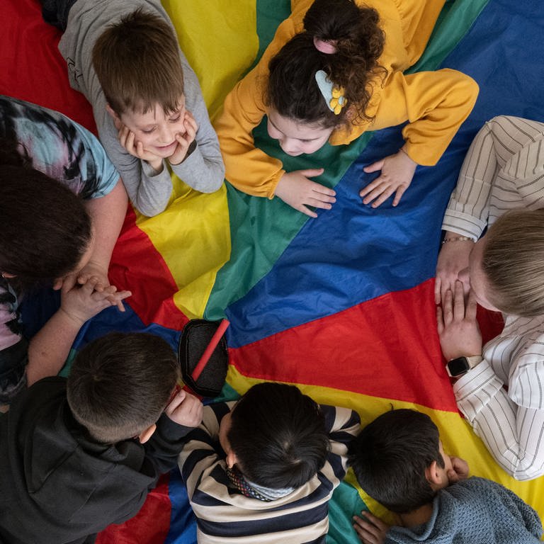 Kindergartengruppe und Erzieherinnen liegen zusammen auf einem großen Tuch 