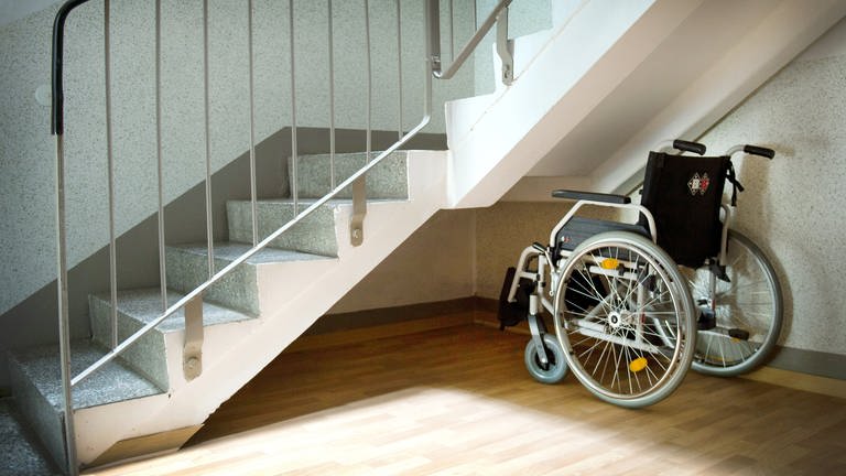 Ein Rollstuhl steht unter einer Treppe