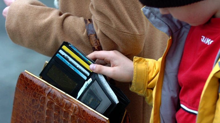 Ein Junge stiehlt eine Geldbörse aus einer Handtasche