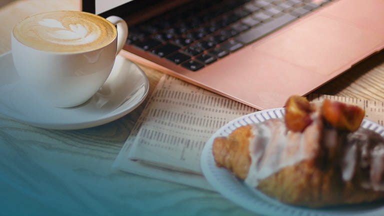 Ein Croissant und ein Café stehen auf einem Tisch vor einem Laptop